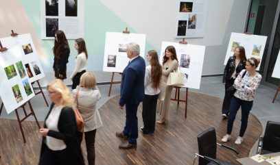 Kilka osób ogląda wystawę fotografii wystawioną na sztalugach.