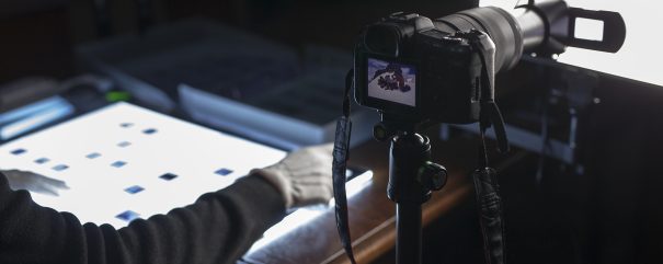 Rozłożone na podświetlanym blacie fragmenty z kliszy aparatu. Obok aparat.