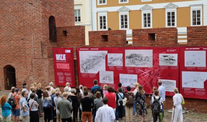 Tłum ludzi ogląda plansze wystawy wywieszone na murach.
