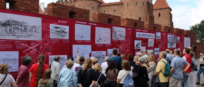 Tłum ludzi ogląda plansze wystawy wywieszone na murach.