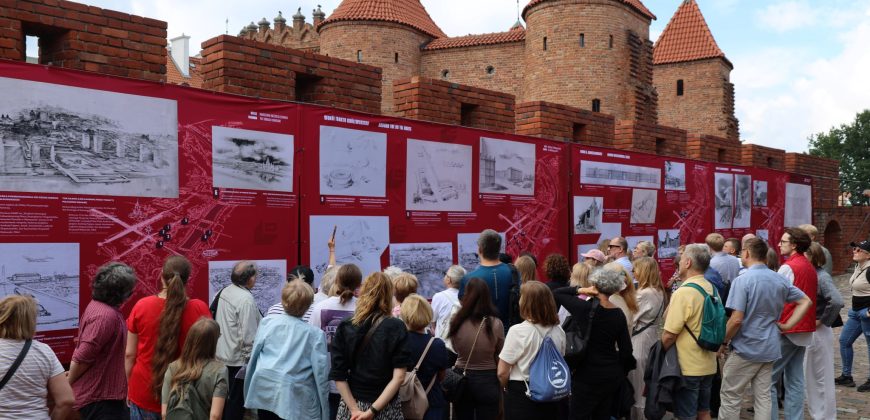 Tłum ludzi ogląda plansze wystawy wywieszone na murach.