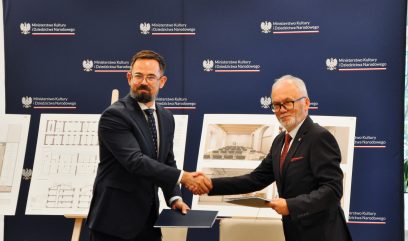 Prezes Baran i dyrektor Zawilski siedzą podają sobie ręce.