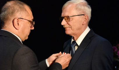 Sekretarz Województwa przypina Andrzejowi Jabłońskiemu odznaczenie do marynarki.