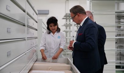 Magazyn archiwalny. Dyrektor Pietrzyk i Matuszak oglądają dokument w wysuniętej szufladzie.