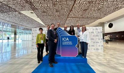 Naczelny Dyrektor wraz z kilkoma innymi osobami stoi przy banerze z logiem Międzynarodowego Kongresu Archiwów na niebieskim dywanie. Za nimi znajduje się ścianka z logiem Kongresu.