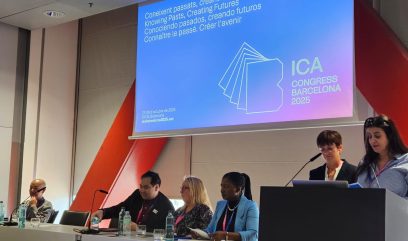 Wyświetlona prezentacja na projektore, pod nim cztery osoby siedzą. Z prawej strony znajduje się mównica, na której przemawiają dwie prelegentki