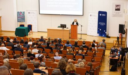 Aula wykładowa. Anne J. Gilliland przemawia do mikrofonu. Przed nią siedzi publiczność.