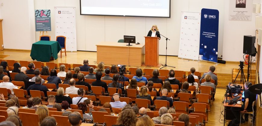 Aula wykładowa. Anne J. Gilliland przemawia do mikrofonu. Przed nią siedzi publiczność.