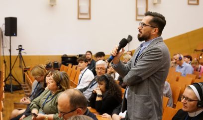 Publiczność siedzi na auli. Mężczyzna z publiczności zadaje pytanie.