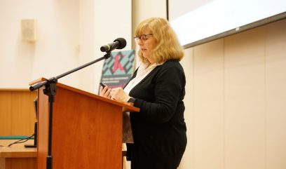 Aula wykładowa. Anne J. Gilliland na scenie przemawia do mikrofonu.