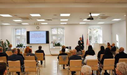 Dyrektor Pietrzyk stoi przed publicznością i przemawia do trzymanego w dłoni mikrofonu.