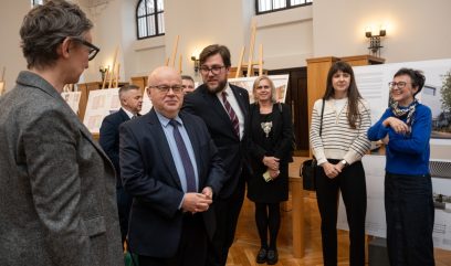 Dyrektor Wojtkowski w otoczeniu 7 osób. W tle plansze z wystawą.