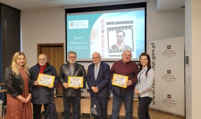 Sześć osób stoi w pomieszczeniu, niektóre trzymają certyfikaty w żółtych ramkach, przed ekranem prezentacyjnym z napisem 