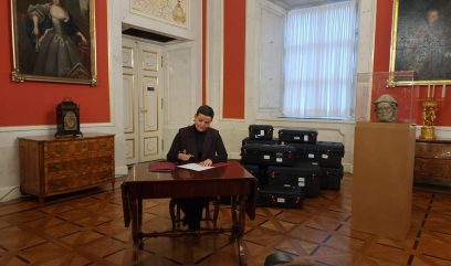 Ministra siedzi przy stoliku i podpisuje dokumenty.