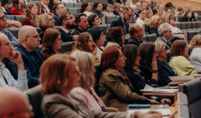 Duża grupa ludzi siedzi blisko siebie w audytorium na Kongresie Strategicznym, uważnie oglądając prezentację lub wykład. Większość patrzy przed siebie, a niektórzy robią notatki. Atmosfera wydaje się profesjonalna, a uczestnicy ubrani są w stroje biznesowe.