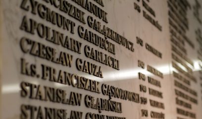Zbliżenie marmurowej ściany pamiątkowej z kilkoma nazwiskami wyrytymi złotymi literami, w tym 