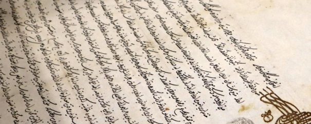Zbliżenie starego manuskryptu z pochyłym, płynnym pismem arabskim zapisanym czarnym atramentem na pożółkłym papierze. W prawym dolnym rogu znajduje się ozdobna kaligraficzna pieczęć i zaokrąglony szary odcisk palca lub pieczęć. Dokument wykazuje pewne plamy i plamy starcze.