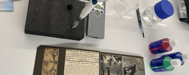Na białym stole laboratoryjnym leżą rozłożone strony starego polskiego czasopisma Przegląd Fotograficzny z czarno‑białymi zdjęciami; obok znajduje się szara piankowa podkładka z zamocowaną sondą i miernikiem pH METTLER TOLEDO, przezroczysta zlewka, pipeta oraz kilka butelek z kolorowymi płynami i niebieskimi zakrętkami.