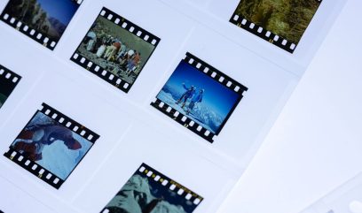 Przezroczysty arkusz z kilkoma slajdami 35 mm ułożonymi w plastikowej koszulce, każdy z czarną perforowaną ramką i miniaturowymi zdjęciami przedstawiającymi ludzi w górach, śnieg i krajobrazy.