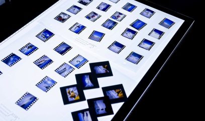 Podświetlona biała płaszczyzna lightboxa z uporządkowanymi w rzędach małymi slajdami filmowymi w czarnych ramkach z perforowanymi krawędziami przedstawiającymi głównie błękitne, ośnieżone pejzaże oraz kilkoma luźnymi ramkami slajdów ułożonymi na środku.