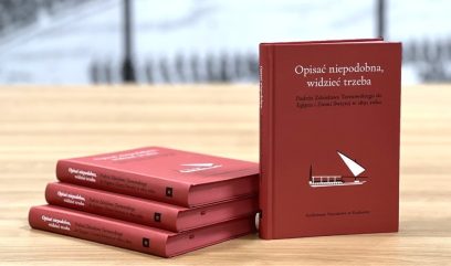 Cztery czerwone twarde książki na jasnym drewnianym stole — trzy ułożone poziomo po lewej i jedna stojąca po prawej, na stojącej okładka z tytułem 