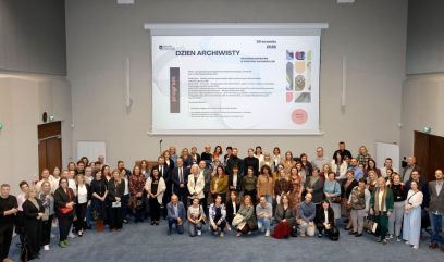 Duża grupa osób ustawiona w rzędach w sali konferencyjnej przed rzutnikiem i dużym ekranem z napisem 